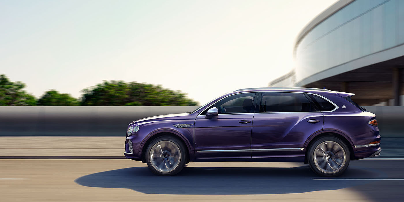 Bentley Santo Domingo Bentley Bentayga Extended Wheelbase Mulliner luxury SUV profile in Tanzanite Purple paint, driving on an country road past trees.
