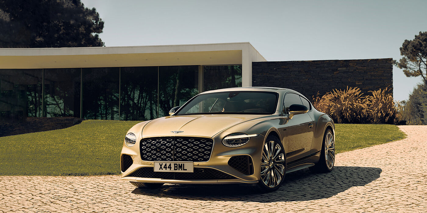 Bentley Santo Domingo Bentley Continental GT Mulliner coupe front three quarters in Patina paint parked outside a glass fronted building with a grass lawn behind it