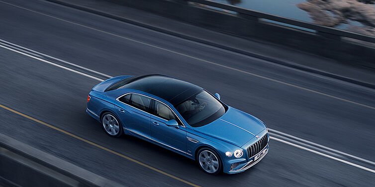 Bentley Santo Domingo New Bentley Flying Spur Azure sedan in Light windsor blue paint by Mulliner, with 22 inch Azure wheels seen from overhead driving dynamically on a country road