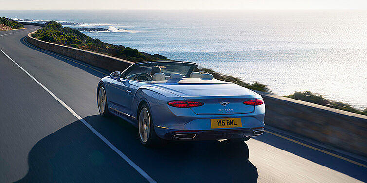 Bentley Santo Domingo New Bentley Continental GTC Azure convertible rear view in Light Windsor blue paint with 22 inch ten spoke wheels driving dynamically on an ocean road in the sunshine